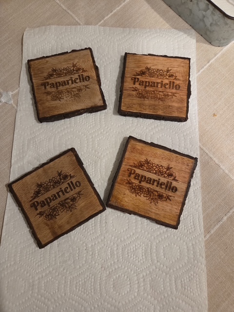 Four rustic wooden coasters engraved with the name Papariello surrounded by floral line art