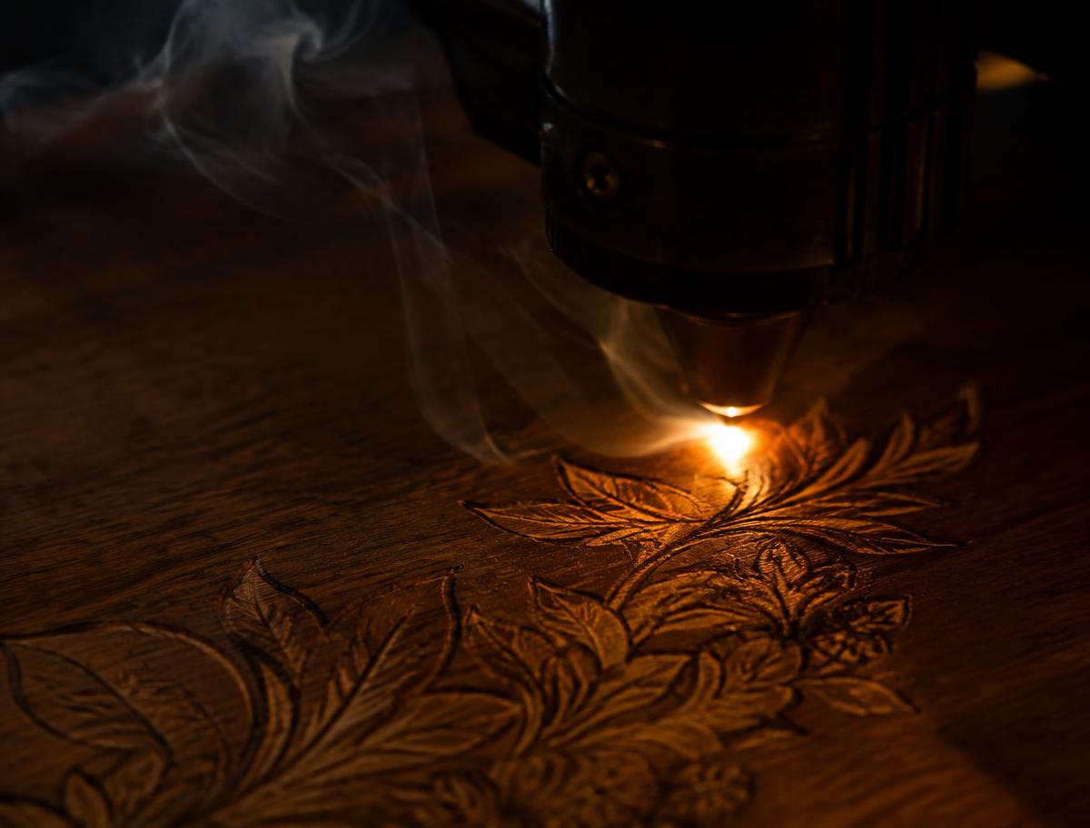 Illustrative concept: a floral pattern being engraved into dark wood under warm light